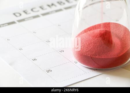 Hourglass on December calendar marking 25th December, countdown to Christmas, red sand running through bulbs of hourglass measuring the passage of tim Stock Photo