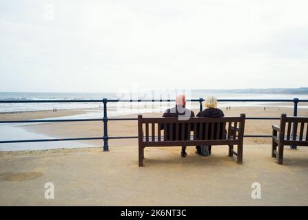 An older couple sitting on a bench looking out over Filey bay in North Yorkshire Stock Photo