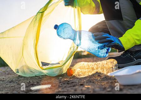 Man's hands pick up plastic bottles, put garbage in green garbage bag to clean up at city, avoid pollution, be friendly to the environment and ecosyst Stock Photo