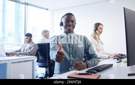 Thanks for calling the best. a young businessman using a headset and showing thumbs up in a modern office. Stock Photo