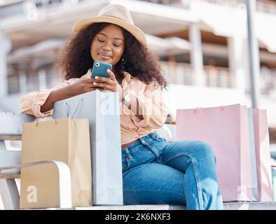 Phone, shopping and happy black woman with shop and store bags on a bench outdoor. Online, mobile and ecommerce app scroll of a young person smile Stock Photo