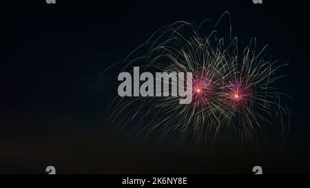 Close up of fireworks explosion with pink stars and yellow fountains. Isolated on black night sky. Ideal for Sylvester and New Year. Stock Photo