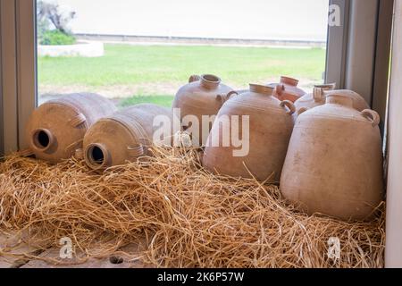 Clay jugs, amphorae and water vessels on straw near a glass window Stock Photo