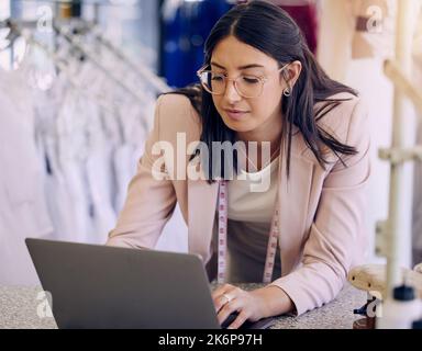 I update my website with new designs regularly. a seamstress using a laptop while working in a boutique. Stock Photo