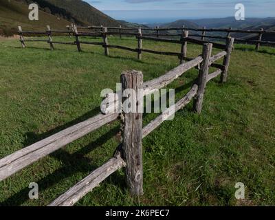 Wood fence in a lush green meadow with valley and mountains in the background. Stock Photo