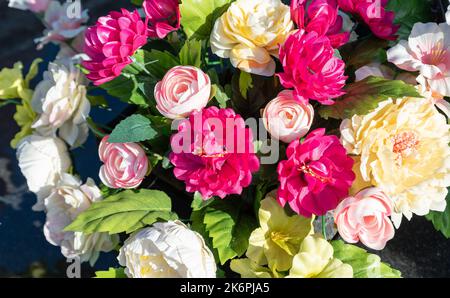 Bunches of artificial flowers in close-up. Faded artificial flowers on the grave. Colorful flowers on the grave. Stock Photo