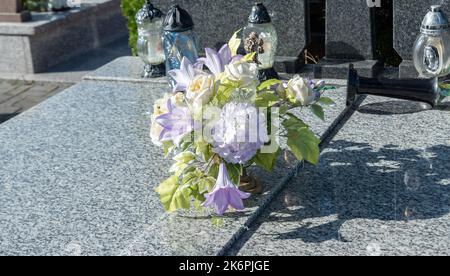 Bunches of artificial flowers in close-up. Faded artificial flowers on the grave. Colorful flowers on the grave. Stock Photo