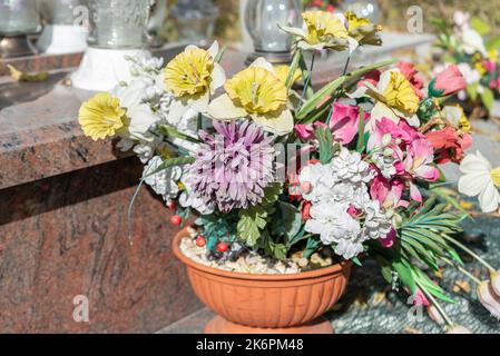 Bunches of artificial flowers in close-up. Faded artificial flowers on the grave. Colorful flowers on the grave. Stock Photo