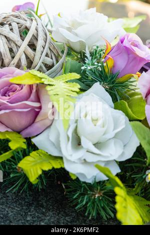 Bunches of artificial flowers in close-up. Faded artificial flowers on the grave. Colorful flowers on the grave. Stock Photo