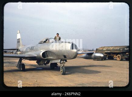 One-half right front view of a Lockheed RF-80A Shooting Star (s/n 45-8365) bearing the markings of the 15th Tactical Reconnaissance Squadron (TRS), somewhere in Korea. A crewman stands on the left wing talking with the pilot in the cockpit. In the background is a North American F-51 Mustang. On the left side of the RF-80A, two Navy aircraft appear in the background. A fuel truck also appears parked parallel to the RF-80A. Stock Photo