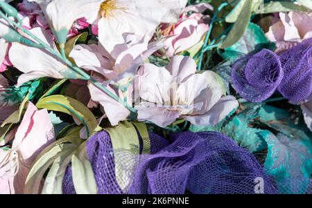 Bunches of artificial flowers in close-up. Faded artificial flowers on the grave. Colorful flowers on the grave. Stock Photo