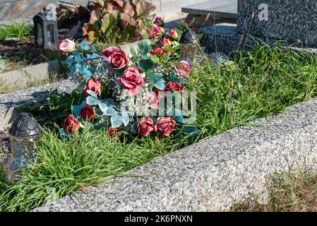 Bunches of artificial flowers in close-up. Faded artificial flowers on the grave. Colorful flowers on the grave. Stock Photo