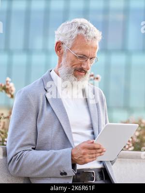Old senior professional business man using digital tablet standing outdoors. Stock Photo