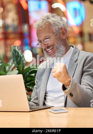 Excited old business man using laptop celebrating winning online bet. Stock Photo