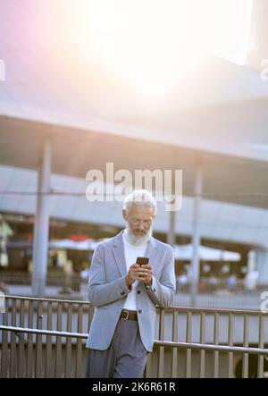 Old senior business man using smartphone standing in city outdoors. Stock Photo