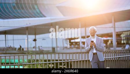 Older mature business man using smartphone standing in city outdoors. Stock Photo