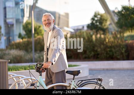 Happy active smiling old senior gray haired man renting bicycle in city park. Stock Photo