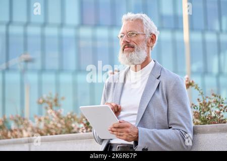 Old senior professional business man using digital tablet thinking outdoors. Stock Photo
