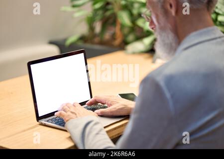 Old senior business man teacher typing on laptop with mockup white screen. Stock Photo
