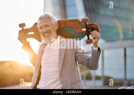 Happy cool older senior business man skater holding skateboard in city. Stock Photo