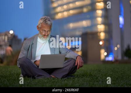 Professional older senior business man using laptop in night city park. Stock Photo