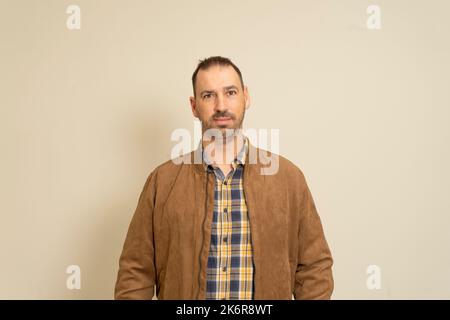 Hispanic man in his 40s with a beard posing smiling wearing a brown jacket, isolated on beige studio background. Stock Photo
