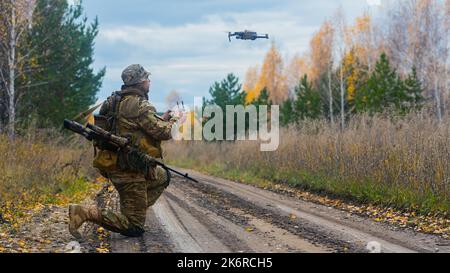 Photo of a mercenary soldier launch a reconnaissance drone on the road in a forest. Modern technological methods of reconnaissance and warfare. Vertic Stock Photo