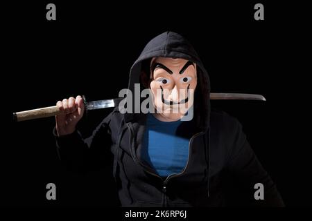 Man armed with a Japanese sword and wearing a mask and a hoodie on black background. Stock Photo