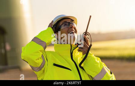 female engineer with safety jacket standing in front of a wind turbine talking in a walkie talkie to checking wind turbine system Stock Photo
