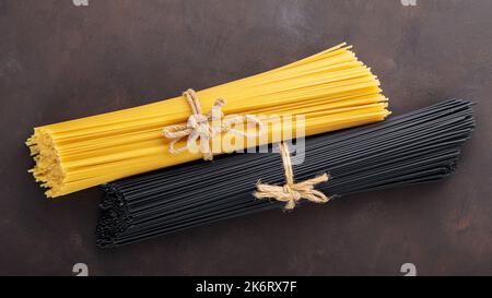 Dry black and yellow pasta spaghetti on dark background. Bunch of raw spaghetti tied with rope. Close-up Stock Photo