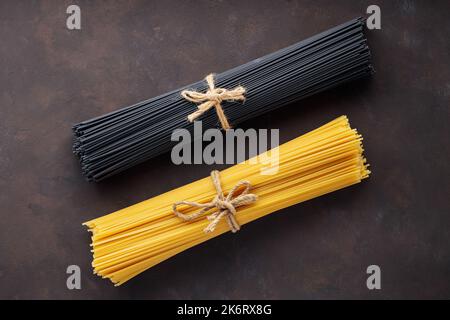 Dry black and yellow pasta spaghetti on dark background. Bunch of raw spaghetti tied with rope. Close-up Stock Photo
