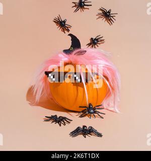 Creative pumpkin in pink wig and 8 bit sunglasses Deal with it. Retro style costume, 80s vibe style. Crawling spiders. Halloween party decoration. Cop Stock Photo