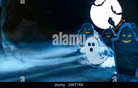Wide Halloween banner with cute ghost flying at night in cemetery between gravestones under the blue light of the moon. Bat silhouettes. Cemetery in t Stock Photo