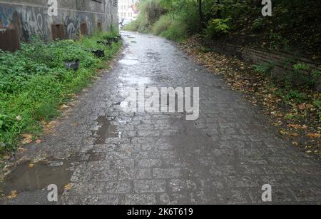 An old wet dirty cobblestone road. Large muddy puddles on the road due to the rainy autumn weather. Stock Photo