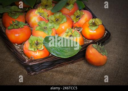Fresh ripe persimmons in a basket on burlap. Stock Photo