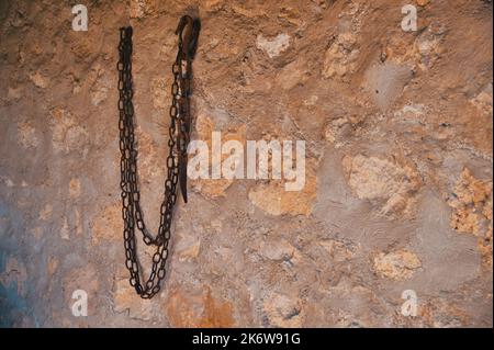 Old rusty iron chain hanging on the stone wall Stock Photo