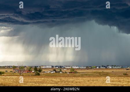 Dark storm clouds over the horizon with heavy rain on a windswept prairie and residential houses in the distance Stock Photo
