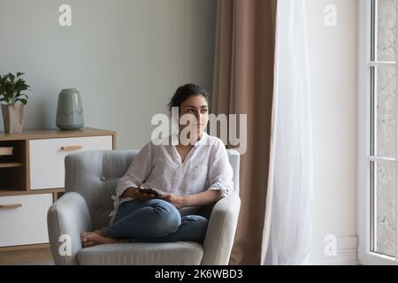 Indian woman resting on cozy armchair staring into distance Stock Photo