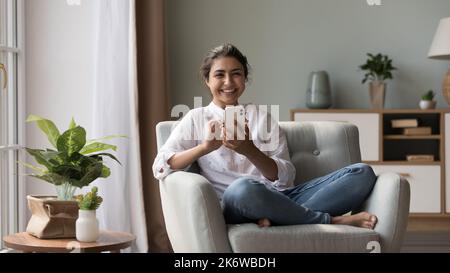 Smiling Indian woman holds modern cellphone looks at camera Stock Photo