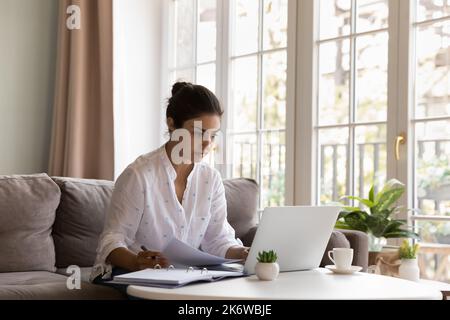 Indian woman doing paperwork or studying at home using laptop Stock Photo