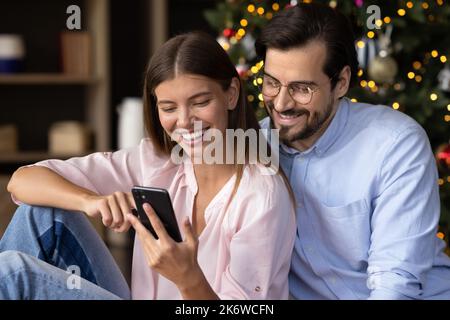 Cheerful young couple sitting together at Christmas tree Stock Photo