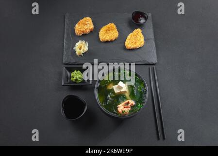 Miso soup with tofu and salmon with onions and sesame seeds. Next to it on a slate, chicken nuggets, Chinese chicken. Set or set of Chinese Asian food Stock Photo