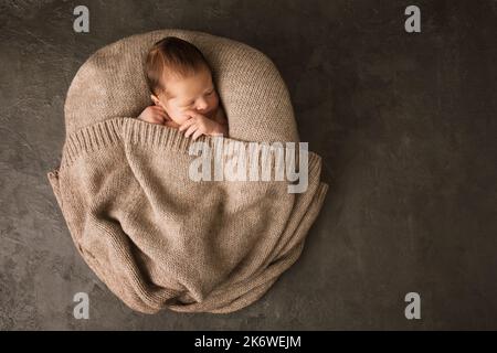 A newborn baby covered with a warm knitted blanket on a dark background Stock Photo