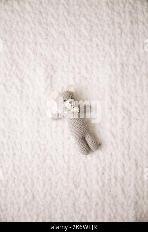 A small toy, a handmade teddy bear knitted from threads on a white blanket Stock Photo
