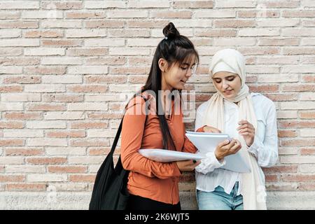 Multi-ethnic female friends studying together while standing outdoors on the street. Stock Photo