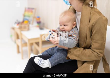 Mother holding infant baby boy in her lap, sitting and waiting in front of doctor's office for pediatric well check. child's health care concept Stock Photo
