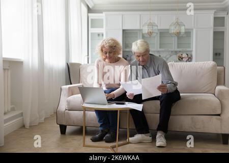 Serious older couple make monthly payments using e-bank on laptop Stock Photo