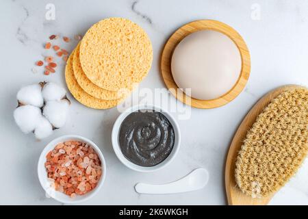 Top view of spa cosmetics products. Clay mask, massage brush with natural bristle, cosmetic sponges, natural soap and himalayan sal to marble table Stock Photo