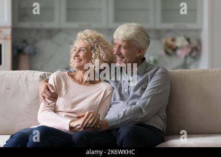 Happy elderly couple relaxing on sofa staring into distance Stock Photo