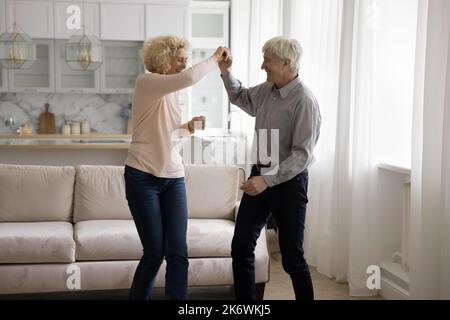 Older couple holding hands dancing together in modern living room Stock Photo